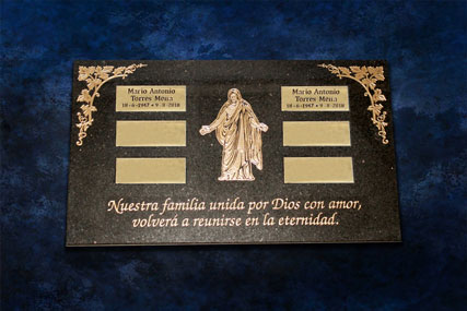 Lápida de granito negro grabada bajo relieve con incrustaciones de latón grabadas con los nombres de los difuntos, imagen de Jesucristo en el medio y esquineras doradas